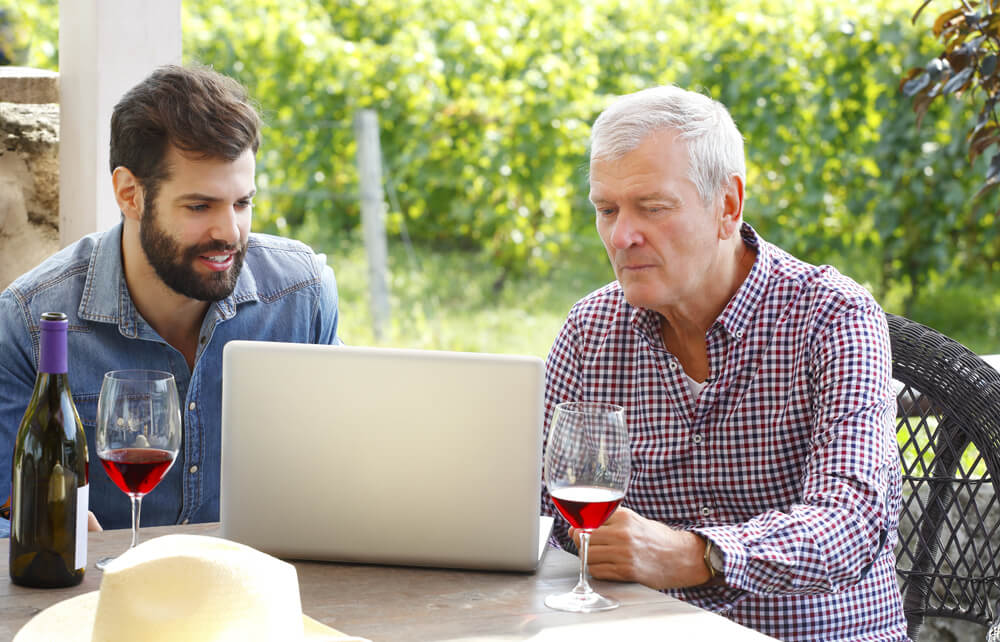 Two men drinking wine while looking at laptop